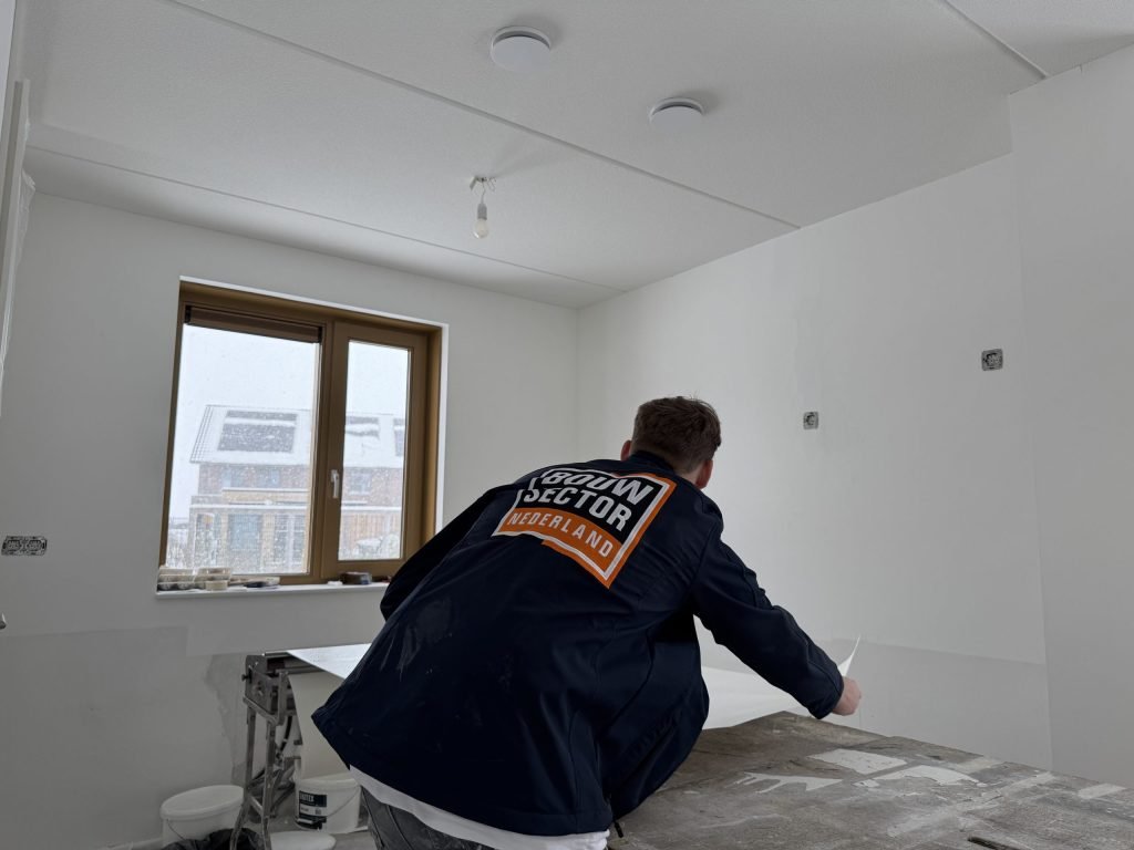 Behanger van Bouwsector Nederland legt een baan vlies klaar op de plaktafel in een kale nieuwbouwkamer