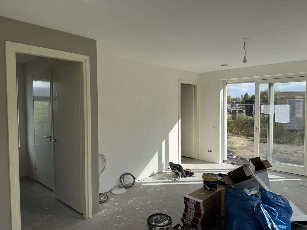 Nieuwbouwwoonkamer tijdens de afwerking, met verfemmers, dozen en materiaal op de vloer