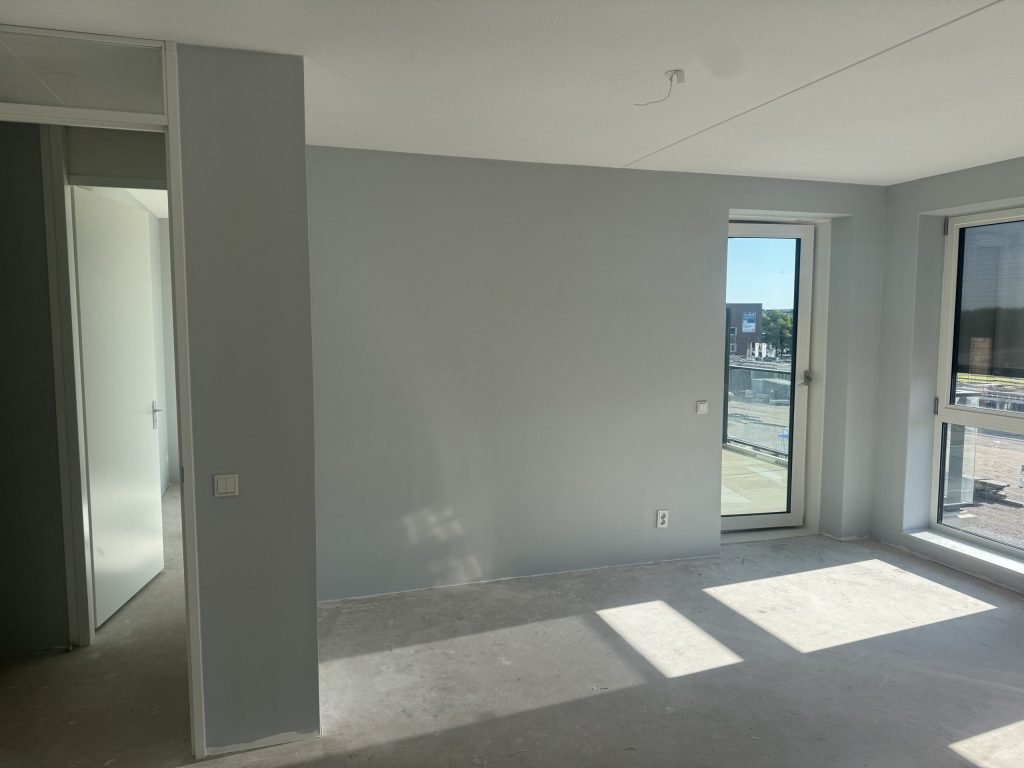 Lege nieuwbouwkamer met egaal afgewerkte lichtgrijze wanden en een betonvloer