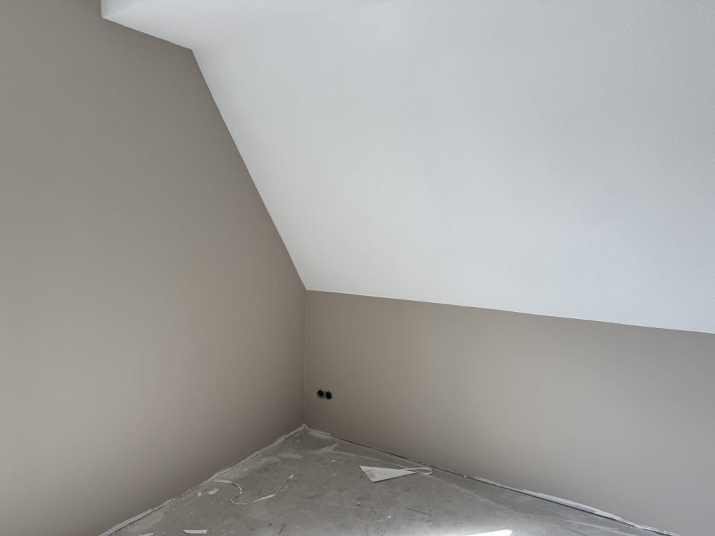 Zolderkamer met een schuine wand, afgewerkt in een warme grijstint en wit