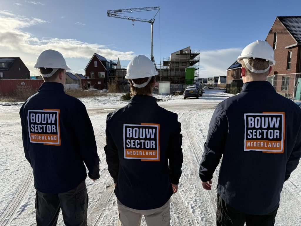 Drie vakmensen van Bouwsector Nederland met witte helm en donkerblauwe jas op een besneeuwde nieuwbouwlocatie